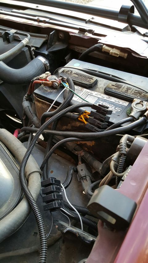 1996 Ford Bronco - A close-up view of a vehicle's engine bay shows a car battery with various wiring harnesses and fuse holders connected to it. The battery i…