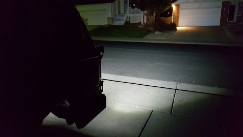1996 Ford Bronco - The rear of a dark colored vehicle is visible in the foreground at night, casting a bright light onto the concrete driveway and asphalt roa…