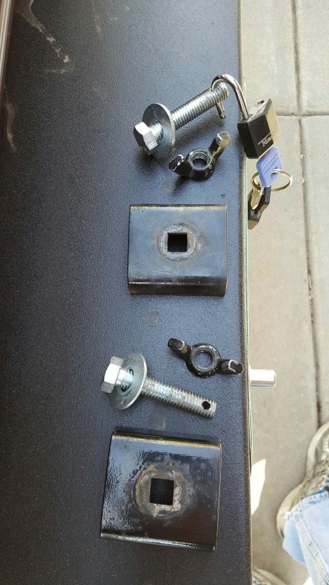 1996 Ford Bronco - Two metal brackets with square cutouts are laid out on a black surface alongside two bolts with washers, two wing nuts, a padlock, and keys…