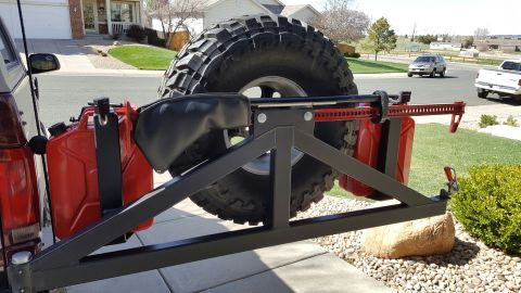 1996 Ford Bronco - A rear-mounted spare tire carrier on a Ford Bronco holds two red jerry cans and a Hi-Lift jack. The vehicle is parked in a driveway with a…
