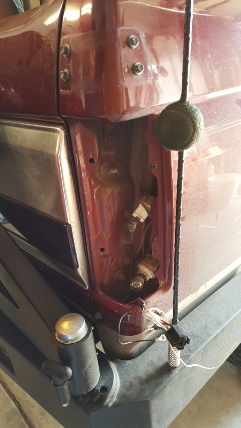 1996 Ford Bronco - The rear passenger side of a red Ford Bronco is shown with the taillight assembly removed, revealing the bulb sockets and wiring. A black a…