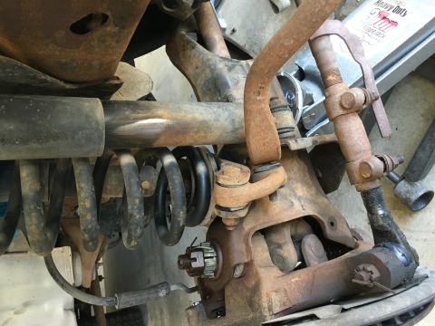 1987 Ford Bronco - A close-up view of the heavily rusted front suspension components of a 1987 Ford Bronco, including the sway bar, coil spring, and steering…