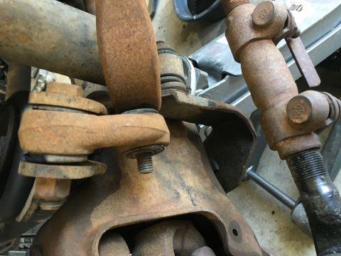 1987 Ford Bronco - This is a close-up, low-angle shot of heavily rusted suspension components on a vehicle. Visible parts include a tie rod end, sway bar link…