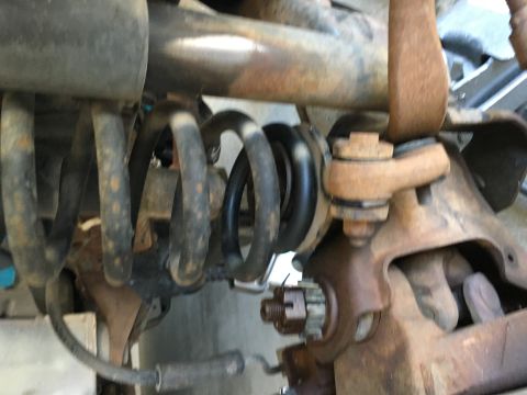 1987 Ford Bronco - A close-up view of the rusty suspension components of a 1987 Ford Bronco, focusing on the coil spring and ball joint assembly. The image sh…