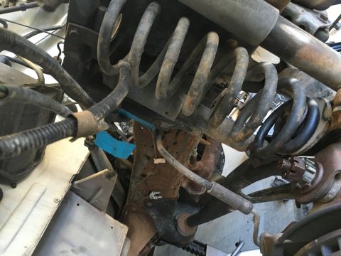 1987 Ford Bronco - A close-up, overhead view of the suspension system of a 1987 Ford Bronco, showing rusty coil springs, brake lines, and wiring harnesses.