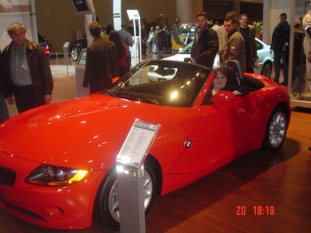 Red BMW Z4 convertible on display with people browsing the auto show floor