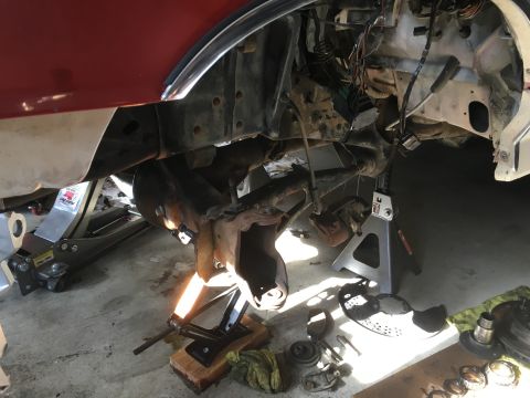 1987 Ford Bronco - The front suspension and brake assembly of a vehicle is disassembled and supported by jack stands and a floor jack. Various brake component…