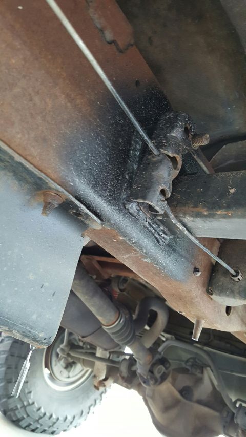 1996 Ford Bronco - Undercarriage view of a 1996 Ford Bronco showing rusted frame components, suspension parts, and a drive shaft. A cable is routed through a…