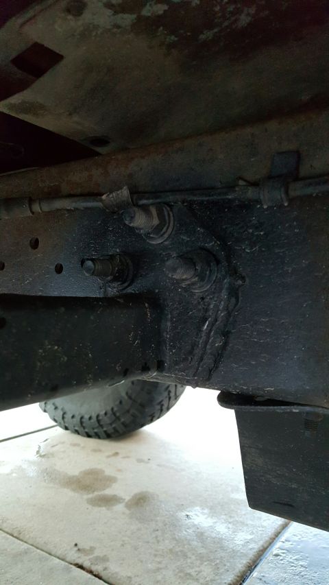 1996 Ford Bronco - A close-up, low-angle shot of the underside of a vehicle's frame, showing several bolts securing a bracket and a portion of a tire and mud…