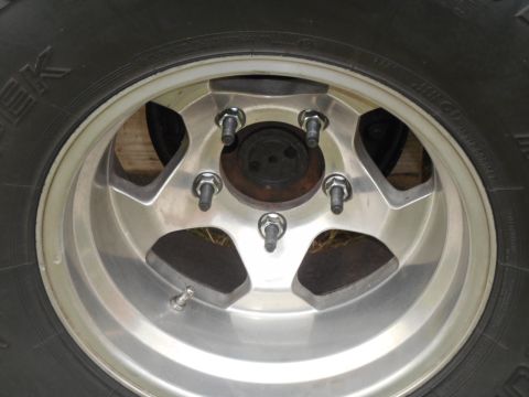 1972 Ford Bronco - A close-up view of a silver five-spoke alloy wheel with lug nuts and a valve stem, mounted on a tire. The wheel is attached to a vehicle th…