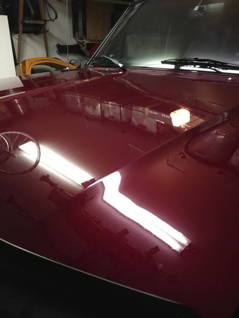 1996 Ford Bronco - The highly polished maroon hood of a classic SUV reflects overhead fluorescent lights and shelving units in a garage. A portion of the wind…