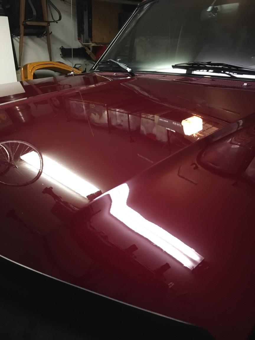 Polished maroon SUV hood reflecting garage interior and lights.