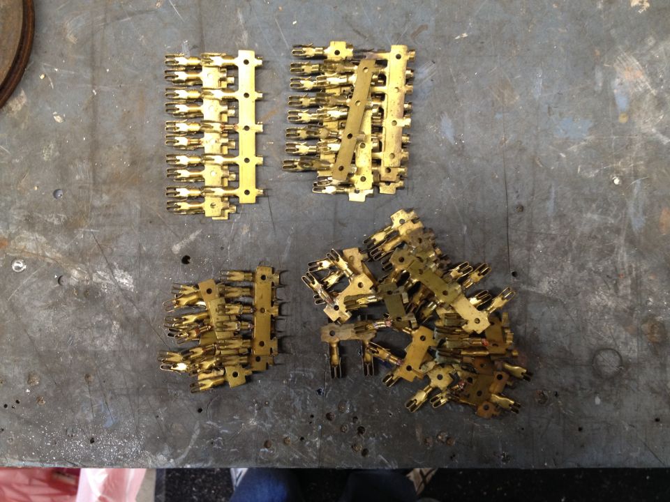 Piles of brass spade terminal connectors on strips lying on a gray metal workbench