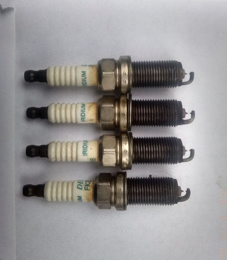 Four NGK Iridium spark plugs arranged horizontally on a white surface.