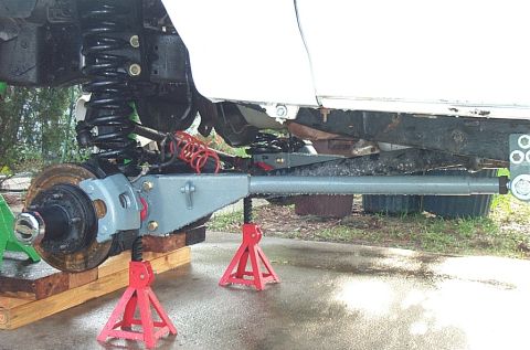 1995 Ford Bronco - Underside view of a vehicle's front suspension raised on two red jack stands, showing a coil spring, drum brake hub, freshly painted gray a…