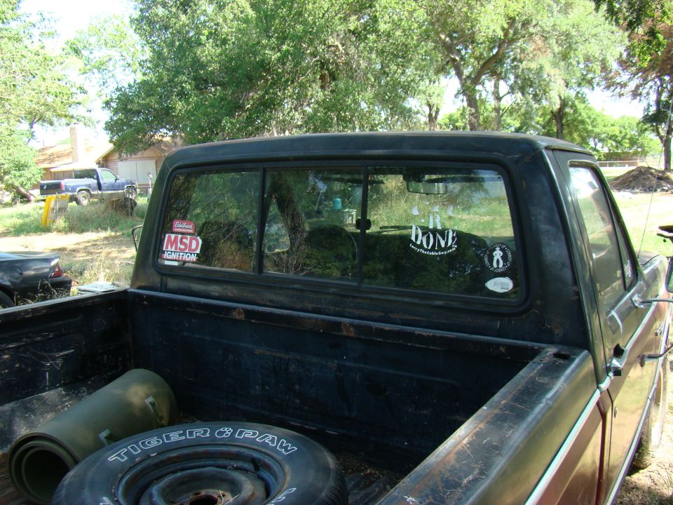 Rear view of a black 1981 Ford F-100 pickup truck with stickers on the window and items in the bed.