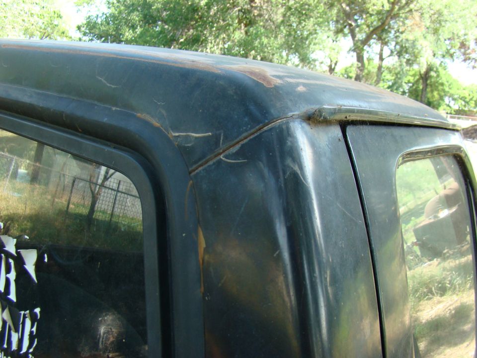 Close-up of a dark truck roofline and rear window frame with rust and scratches.