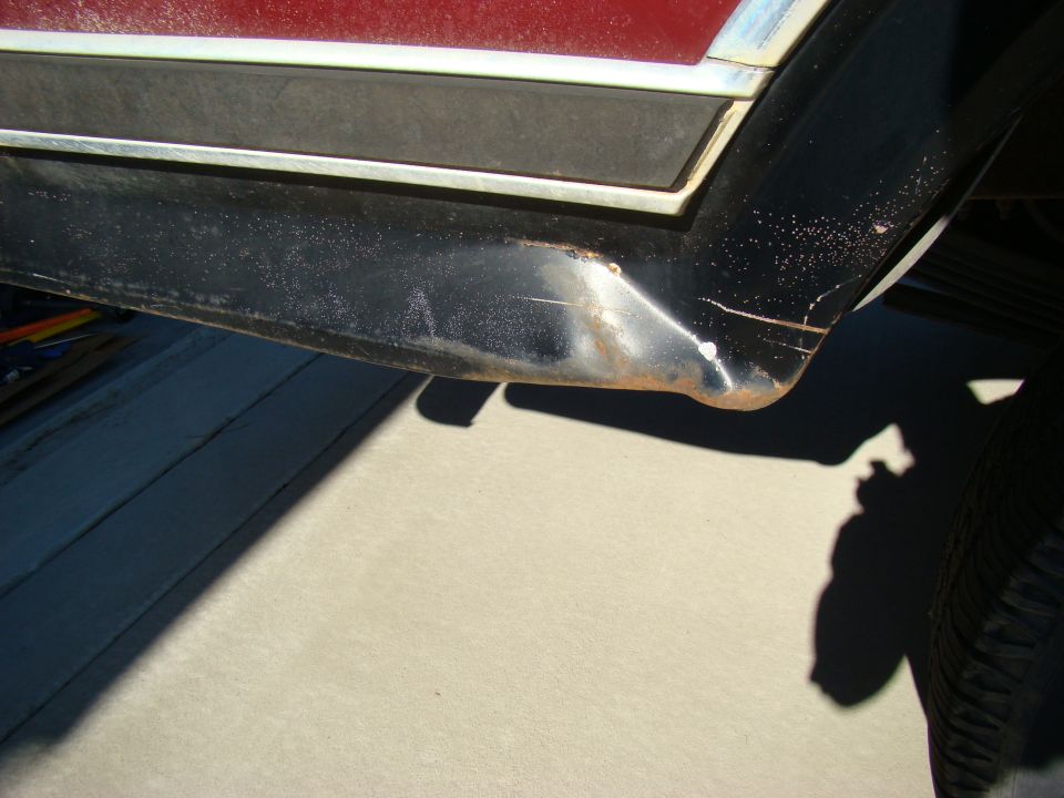 Close-up of damaged black trim on a vehicle fender with rust.