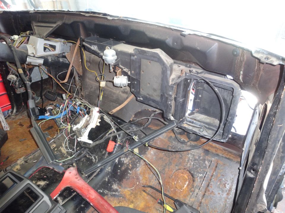 Disassembled dashboard and wiring of a vintage Ford F-100 with rusted floorboards.