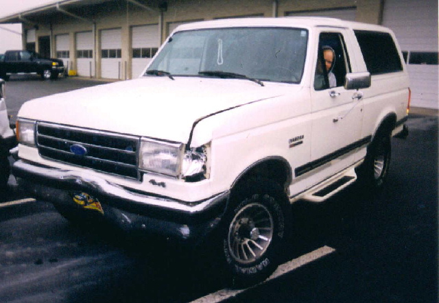 White Ford Bronco SUV with front-end and fender damage, parked in a lot