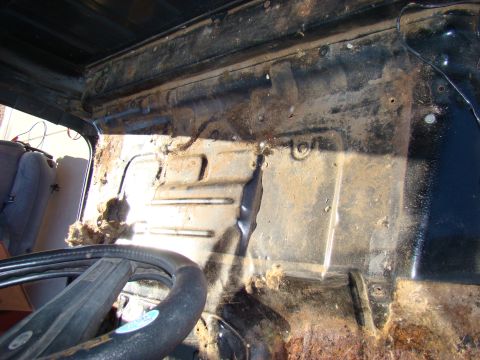 1981 Ford F-100 - Interior view of a rusty and dirty 1981 Ford F-100 cab, showing the floor pan, dashboard area, and part of the steering wheel and driver's…