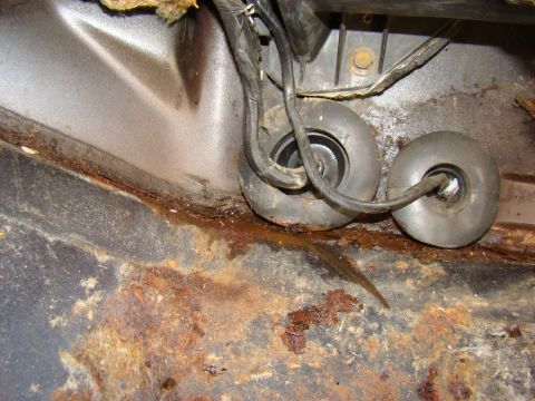 1981 Ford F-100 - This image shows a close-up view of a heavily rusted metal floor panel with two black rubber grommets and wiring. The rust appears to be ex…