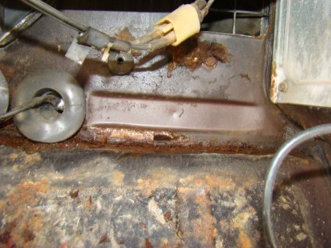 1981 Ford F-100 - Close-up view of heavily rusted metal components, likely from the undercarriage of a vehicle. Wires and circular metal parts are visible am…