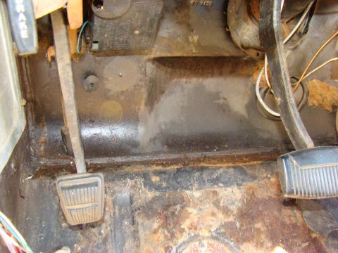 1981 Ford F-100 - The interior floor of a classic Ford truck shows significant rust damage and wear around the brake and clutch pedals. Various wires and a f…