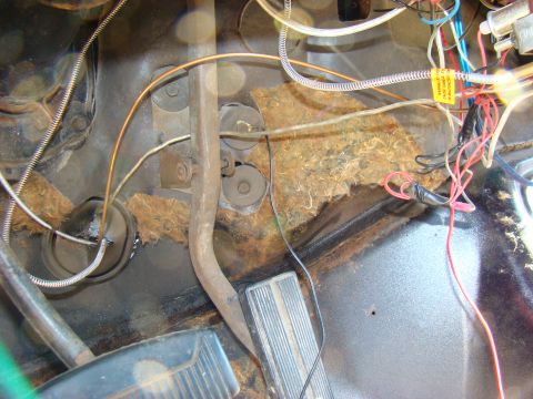 1981 Ford F-100 - The interior floor area of a vehicle shows brake and clutch pedals, wiring, and insulation. The pedals are black with ribbed surfaces, and…