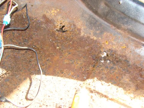 1981 Ford F-100 - The image shows significant rust and a hole in the floor pan of a vehicle, with visible wiring. The surface appears to be the interior floo…