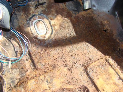 1981 Ford F-100 - The interior floor of a vehicle shows significant rust and corrosion, with a cluster of colorful wires visible in the foreground.