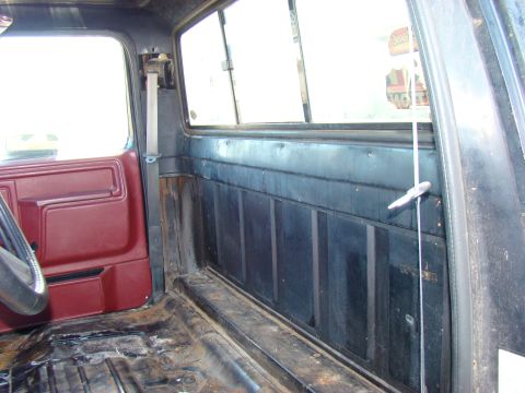 1981 Ford F-100 - Interior view of a pickup truck cab, showing the driver's side door panel, seatbelt mechanism, and the rear wall of the cab.