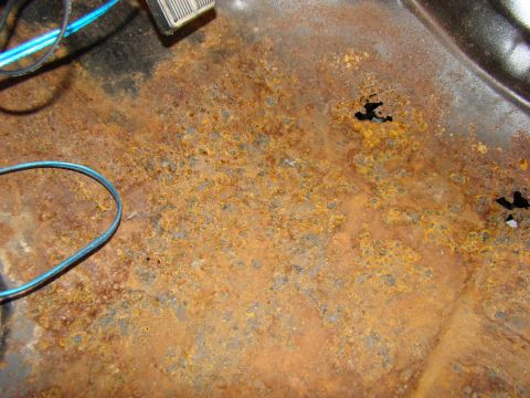 1981 Ford F-100 - This image shows heavily rusted metal, likely the floor pan of a vehicle, with several holes and some blue wiring visible. The texture is r…