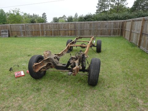 1981 Ford F-100 - A rusty, disassembled 1981 Ford F-100 chassis with wheels is sitting on a grassy lawn in front of a wooden fence. The front suspension and…