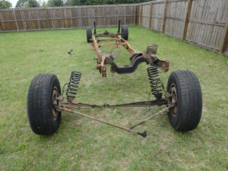 Chassis and front suspension of a classic pickup truck with tires and springs, outdoors.