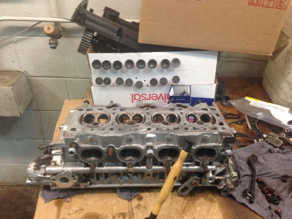 Disassembled engine cylinder head on a workbench with tools and parts.