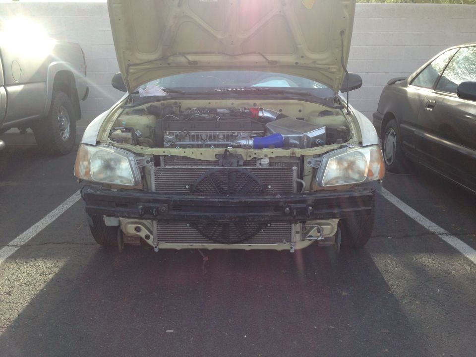 Front view of a modified Hyundai Accent with hood open, showing engine and exposed radiator.