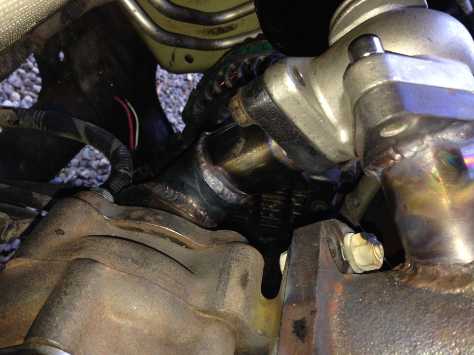 Close-up of vehicle turbocharger and exhaust manifold with visible welds.