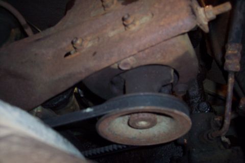 1973 Ford F-250 - A close-up view of a rusty pulley and belt system on a vehicle's engine. The belt is dark and appears to be a V-belt, wrapped around a meta…