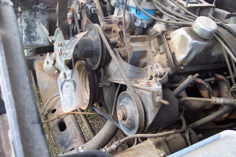 Close-up of rusted V8 engine belts and pulleys in an older Ford truck.