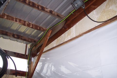 1990 Ford Bronco - This image shows the interior of a structure with a corrugated metal roof supported by wooden beams. A white plastic sheeting covers the wa…