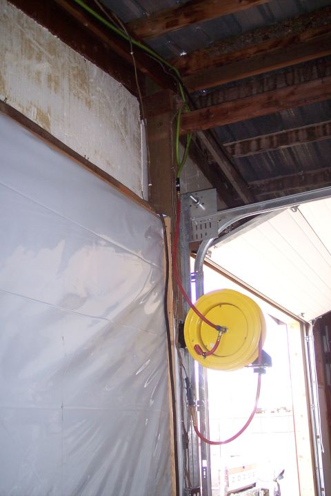 1990 Ford Bronco - A yellow air hose reel is mounted to a metal bracket on a wooden beam in a garage. Green and red hoses are visible, along with part of a ga…