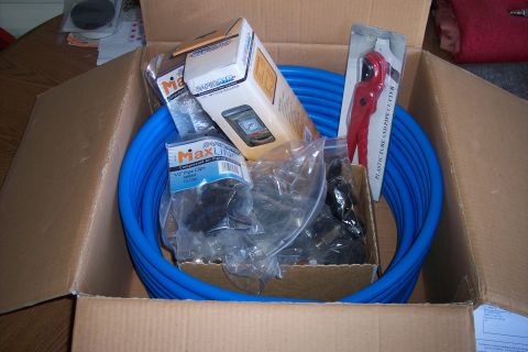 1990 Ford Bronco - An open cardboard box contains a blue coiled tube, a red plastic tube and pipe cutter, and several packages of pipe clips and a regulator.