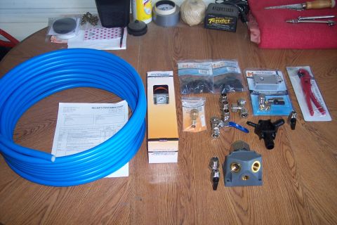1990 Ford Bronco - A collection of air compressor fittings, tubing, and tools are laid out on a wooden surface. Items include a large coil of blue tubing, a r…