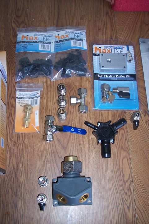 1990 Ford Bronco - A collection of RapidAir Maxline compressed air piping system components are laid out on a wooden floor. The parts include pipe clips, an o…