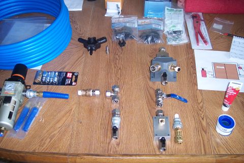 1990 Ford Bronco - A collection of air compressor fittings, tubing, and accessories are laid out on a wooden surface. Items include a blue coiled hose, an air…
