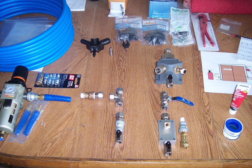 Air compressor fittings, blue hose, regulator, valves, and pipe sealant on a wooden table.