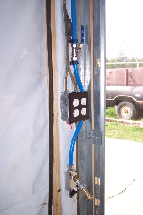 1990 Ford Bronco - A close-up view shows electrical outlets and blue pneumatic tubing attached to a metal frame. A truck is visible in the background through…