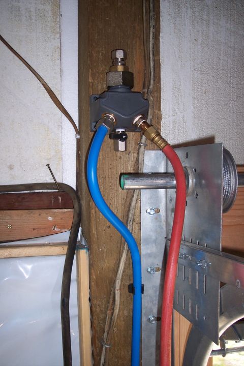 1990 Ford Bronco - This image shows a close-up of plumbing and electrical connections mounted to a wooden post. Two hoses, one blue and one red, connect to a…