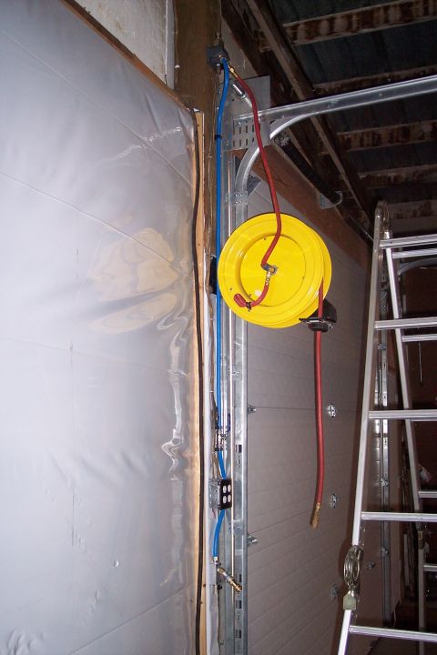 1990 Ford Bronco - A yellow hose reel is mounted on a metal bracket next to a garage door. Blue and red hoses run along the wall, connected to various fitting…
